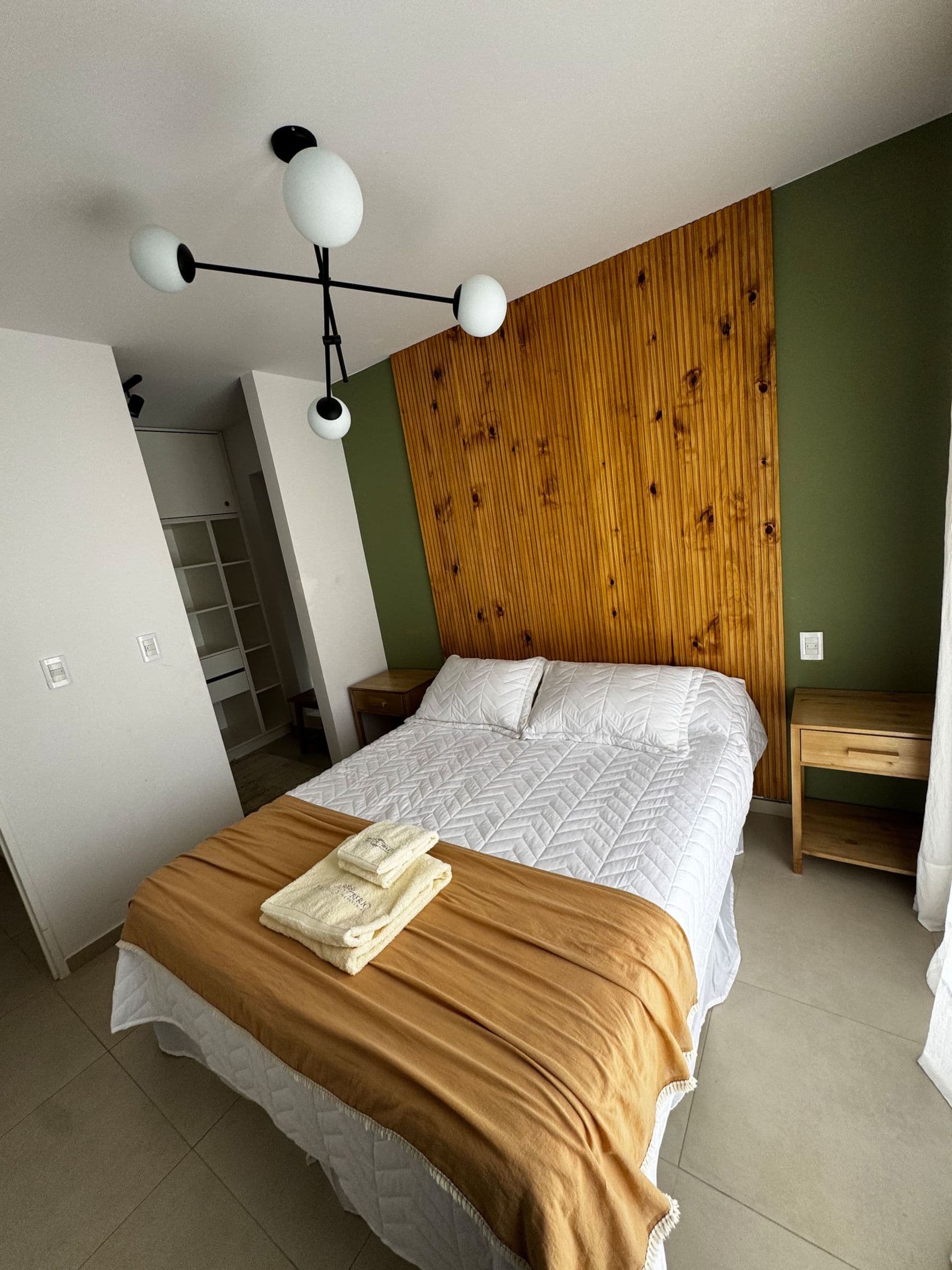 Dormitorio con pared de madera y pared verde, cama doble con manta mostaza